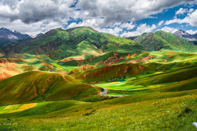 A stunning mountain landscape showcasing vibrant green hills and a winding road under a dramatic sky.