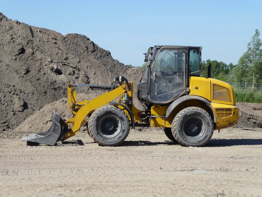 Side view of a yellow loader at a construction site with dirt mounds.