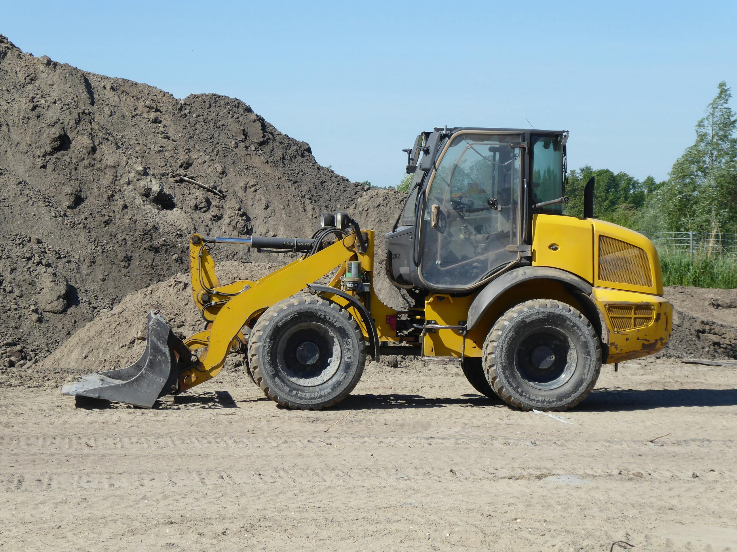 Side view of a yellow loader at a construction site with dirt mounds.